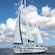 2 people steer a sailing yacht near a populated coastline